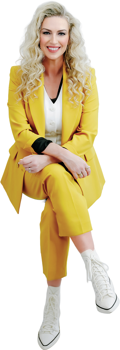 Sara Ross in a yellow blazer and pants sitting down and smiling at the camera